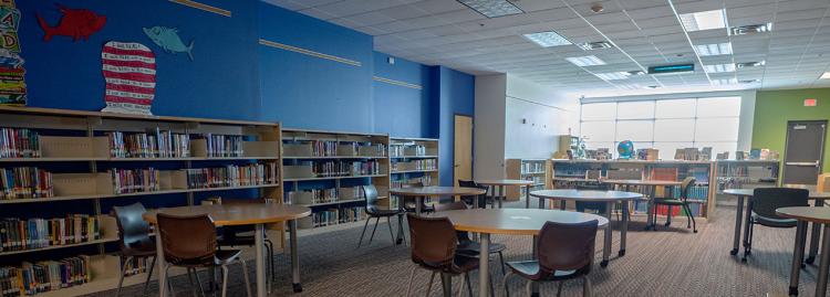 Interior view of library with blue walls, several tables in center and bookshelves on the back wall. 