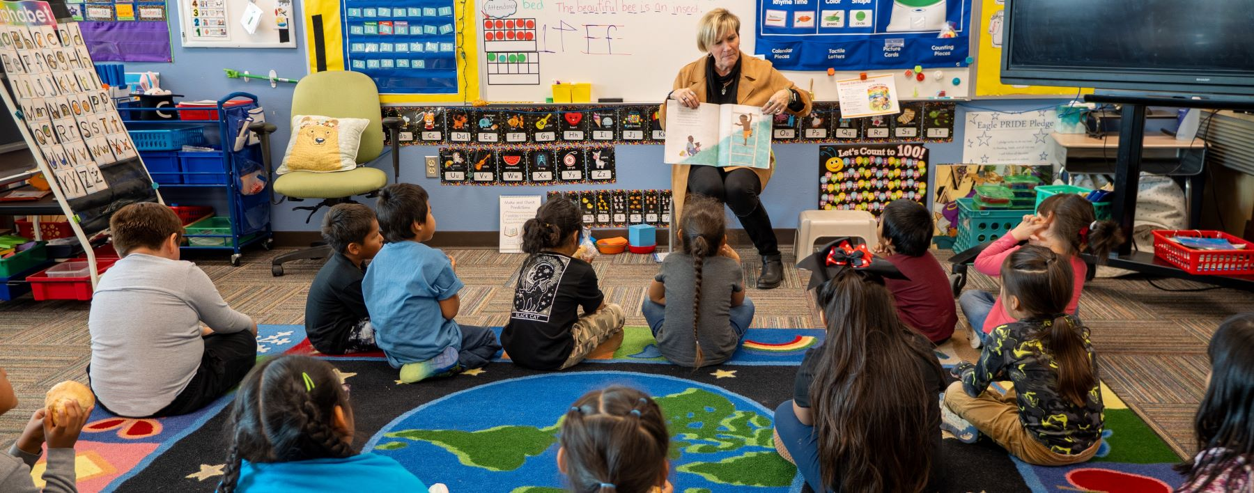 Teacher reading a book a classroom of students. 