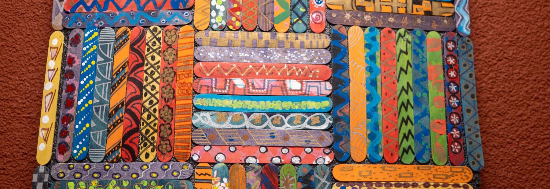 Popsicle sticks painted with different colorful patters and glued together in a weaved patter.