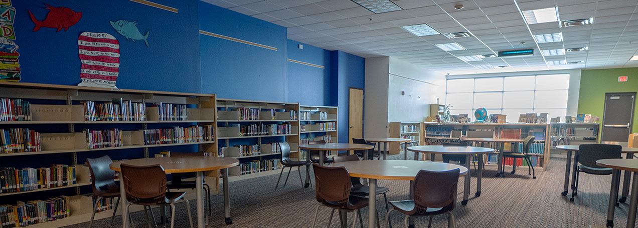 Interior view of library with blue walls, several tables in center and bookshelves on the back wall. 