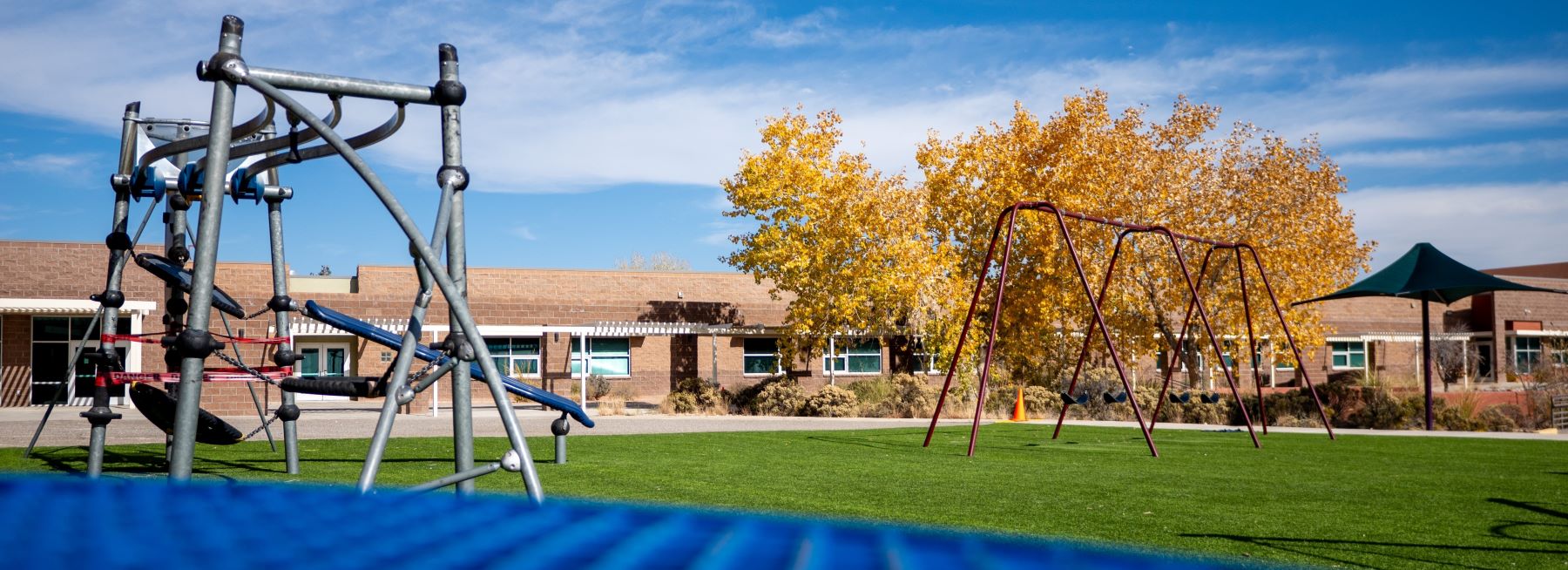 Playground with swings and a slide in front of school building.
