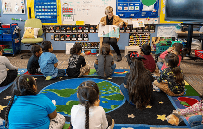 Teacher reading a book to students who are sitting on the floor in the classroom.