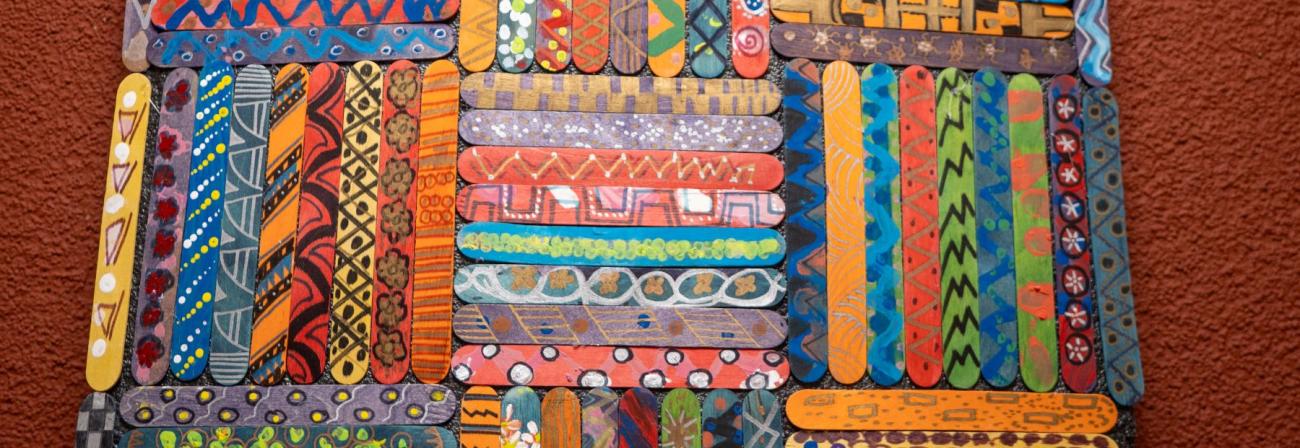 Popsicle sticks painted with different colorful patters and glued together in a weaved patter.