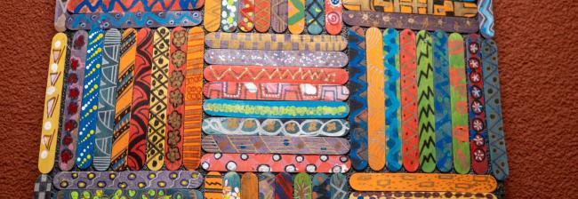 Popsicle sticks painted with different colorful patters and glued together in a weaved patter.